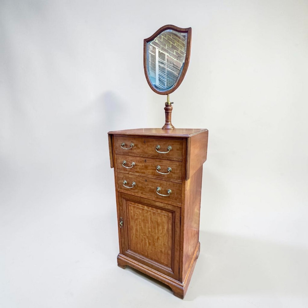 An Edwardian mahogany dressing chest featuring an adjustable shield-shaped mirror, drop-leaf top flaps, three drawers with brass handles, and a lower cupboard. View V