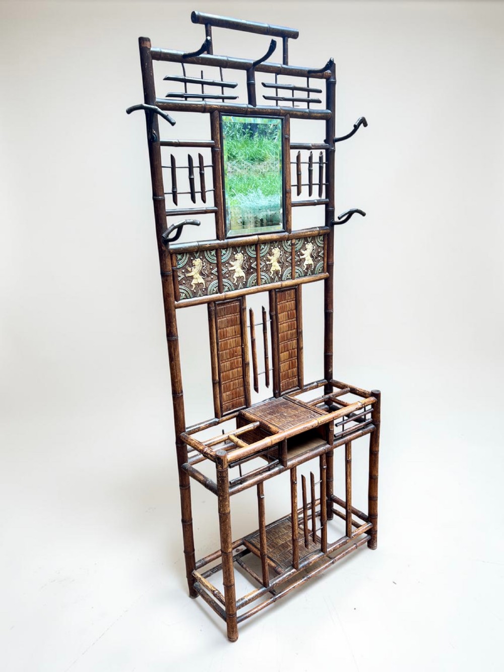 A dark Victorian bamboo hall stand featuring a central mirror, decorative ceramic lion tiles, coat hooks, and integrated umbrella racks.
