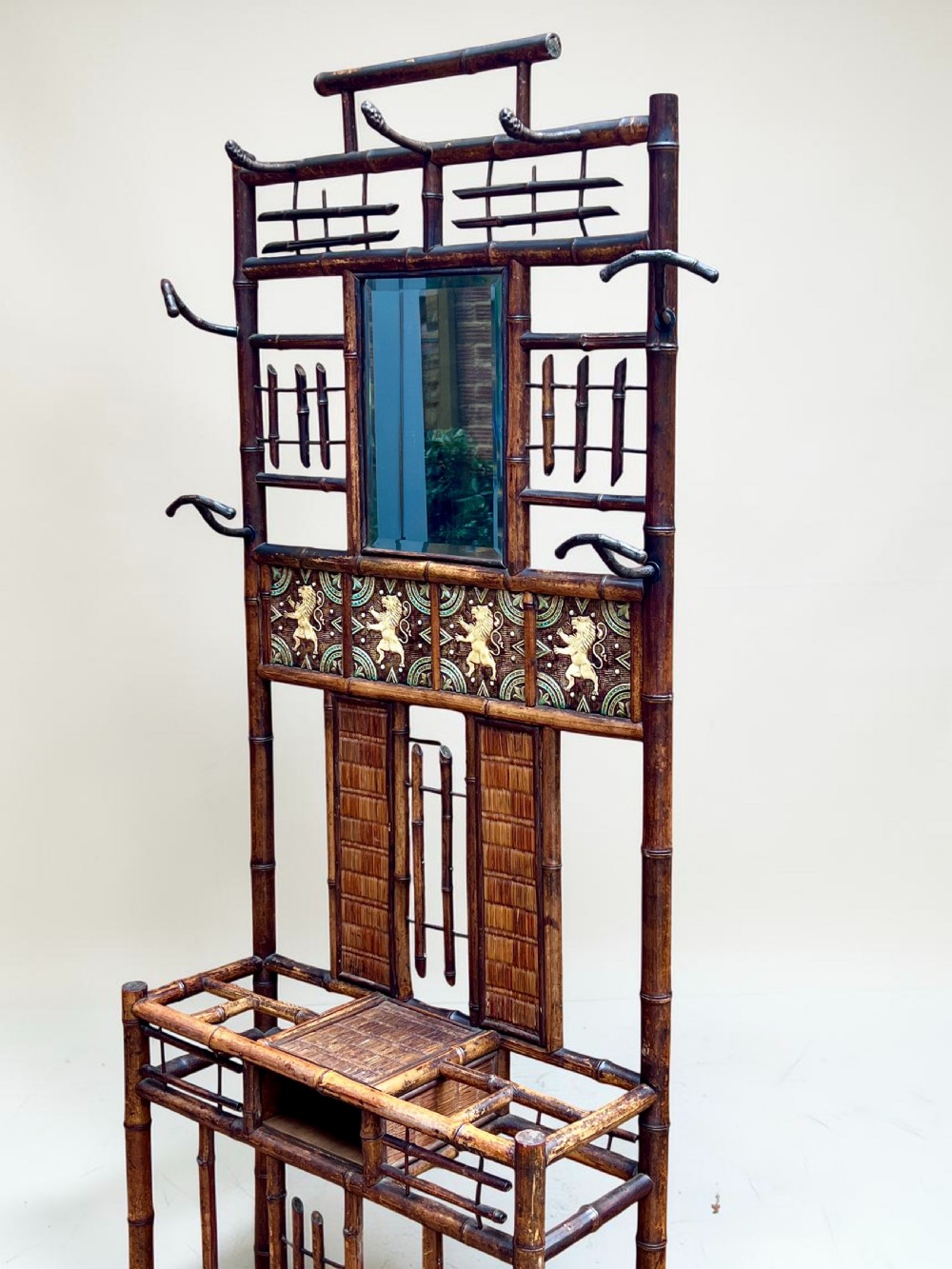 A dark Victorian bamboo hall stand featuring a central mirror, decorative ceramic lion tiles, coat hooks, and integrated umbrella racks. View III