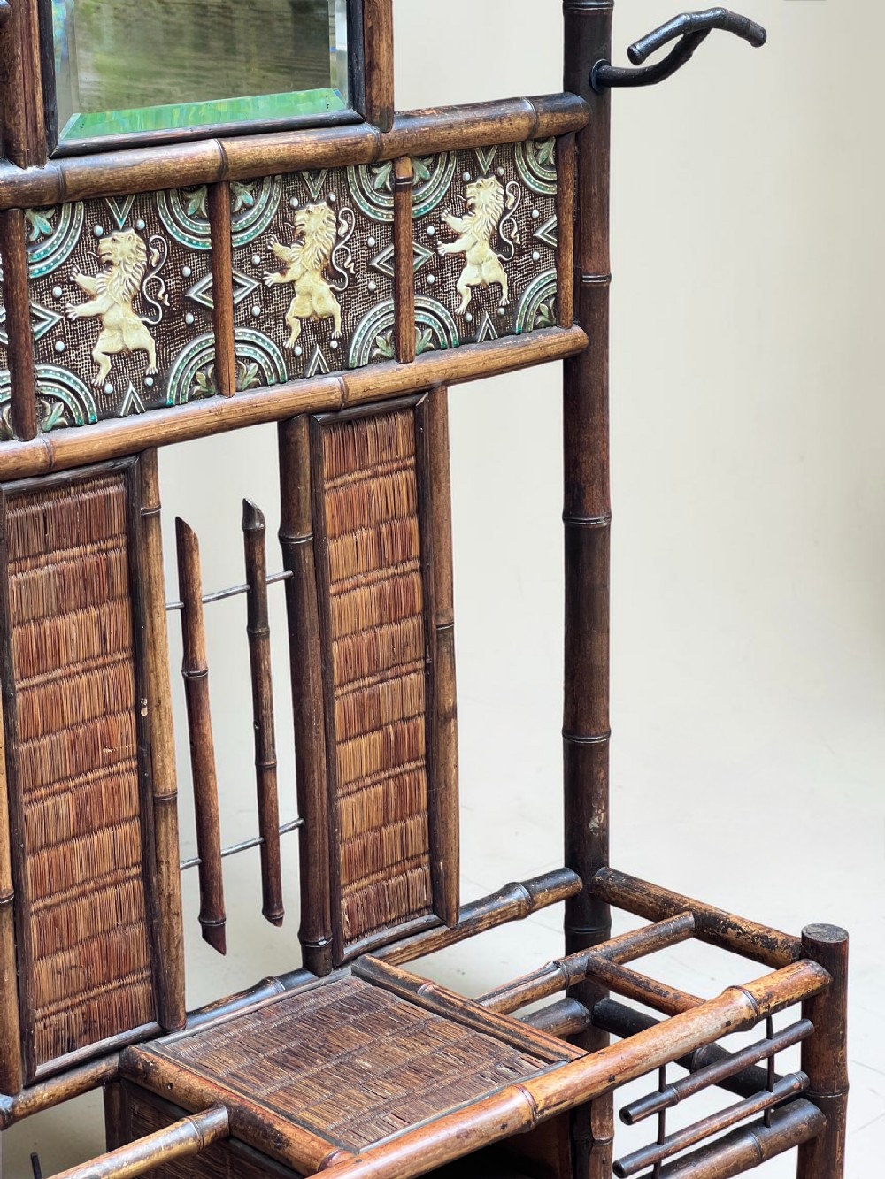 A dark Victorian bamboo hall stand featuring a central mirror, decorative ceramic lion tiles, coat hooks, and integrated umbrella racks. View IV