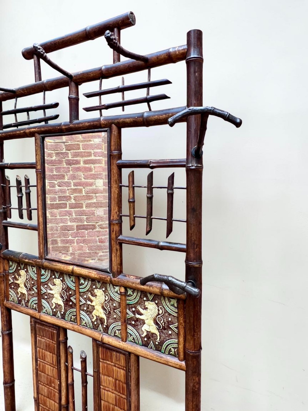 A dark Victorian bamboo hall stand featuring a central mirror, decorative ceramic lion tiles, coat hooks, and integrated umbrella racks. View V