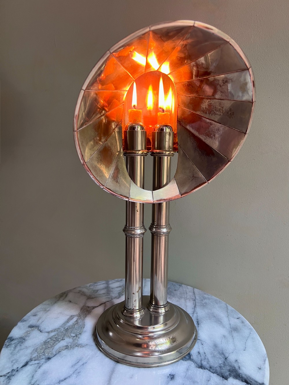 An Edwardian silver-plated candle lamp featuring twin column stems, a curved segmented reflector hood, and an engraved circular base.