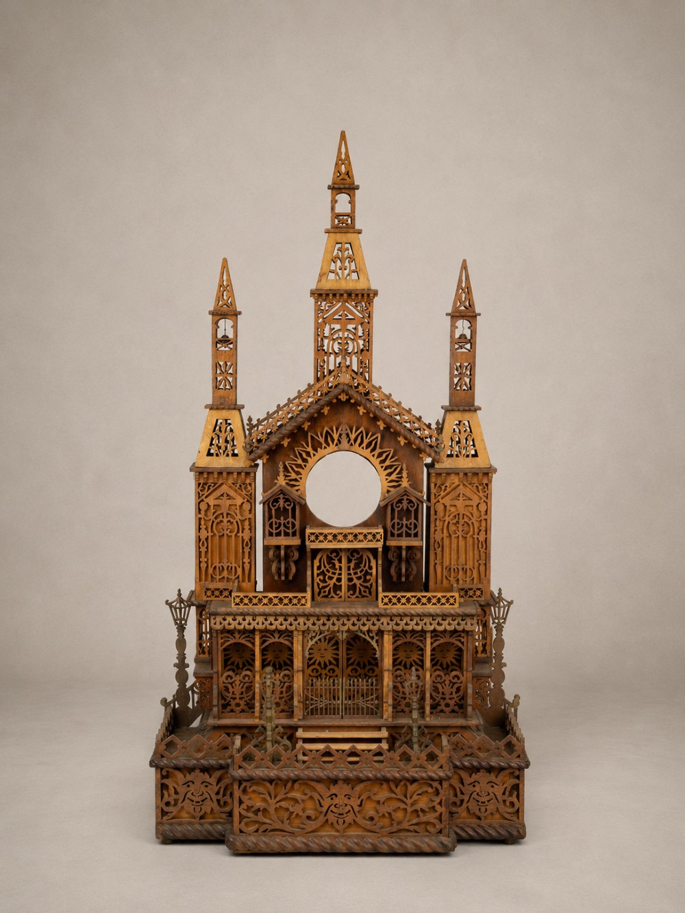 A carved wooden clock case designed in a Gothic cathedral architectural style with detailed fretwork, three spires, and a circular central opening.