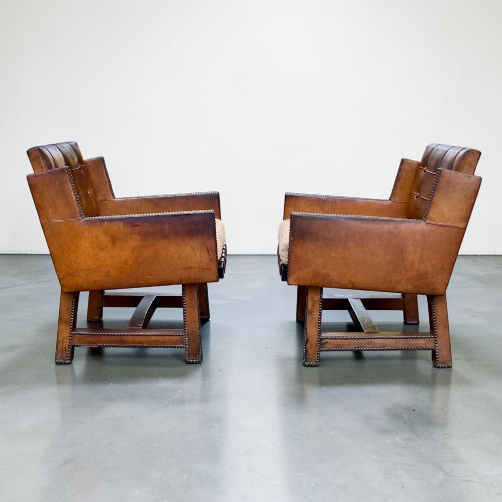 A pair of French 1930s cognac leather button-back armchairs with brass stud detailing and fabric seat cushions on wooden frames. View IV