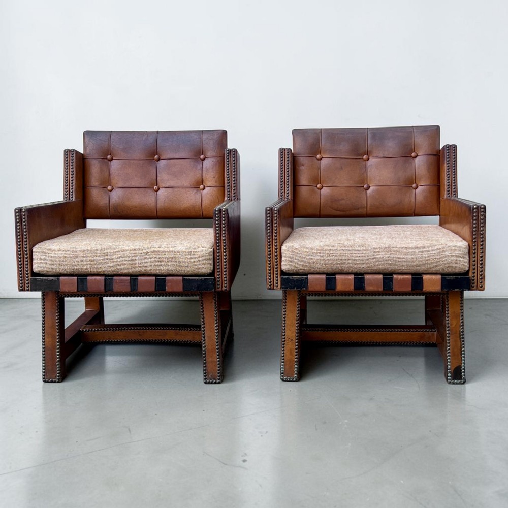 A pair of French 1930s cognac leather button-back armchairs with brass stud detailing and fabric seat cushions on wooden frames. View V