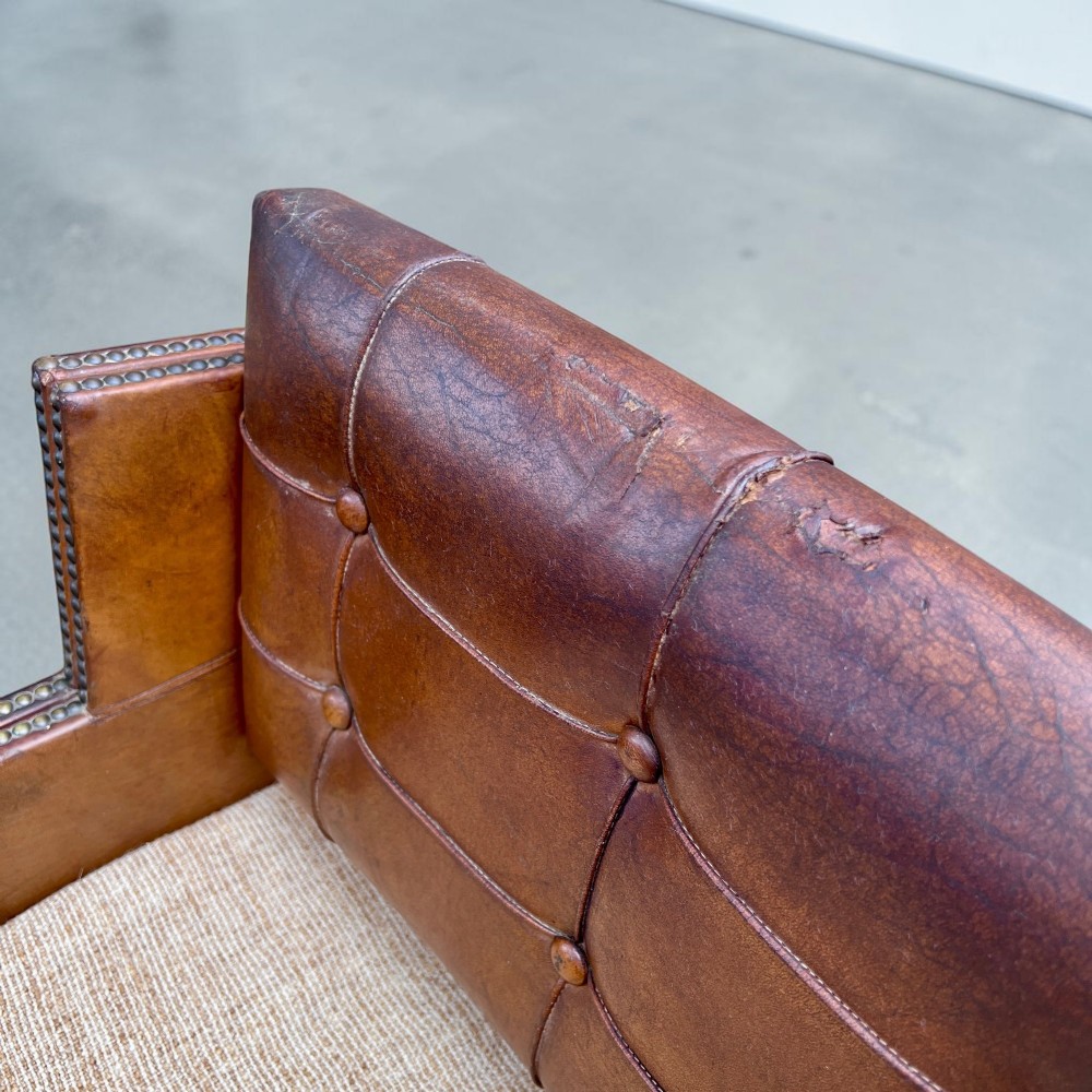 A pair of French 1930s cognac leather button-back armchairs with brass stud detailing and fabric seat cushions on wooden frames. View IX