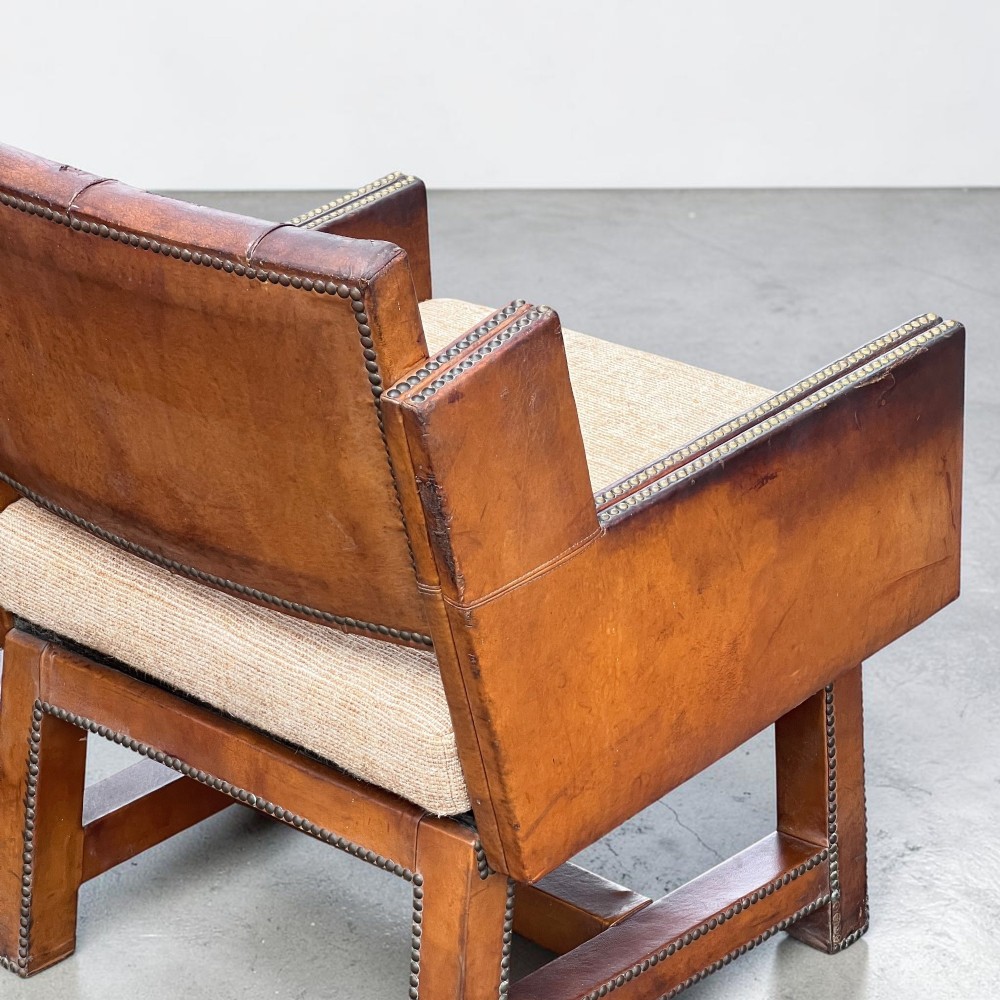 A pair of French 1930s cognac leather button-back armchairs with brass stud detailing and fabric seat cushions on wooden frames. View X