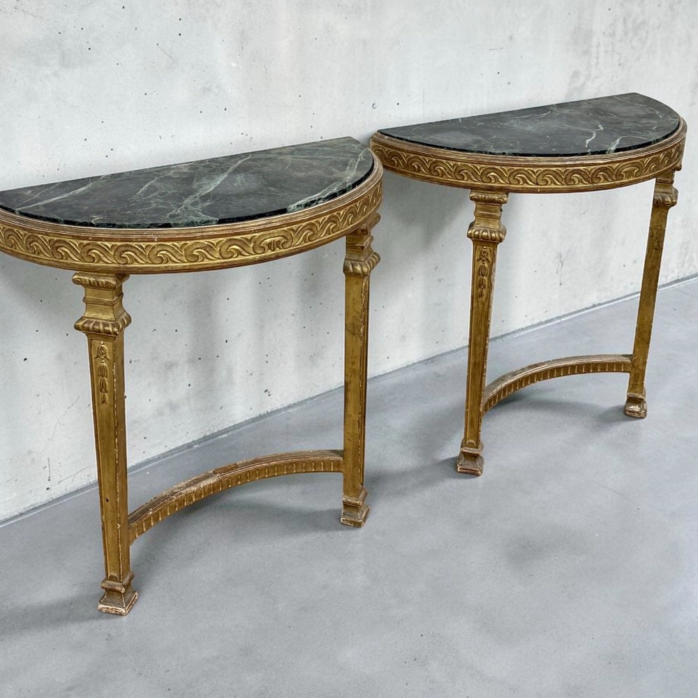 A pair of 19th-century Louis XVI Revival demilune console tables with carved gold giltwood frames and dark green marble tops.