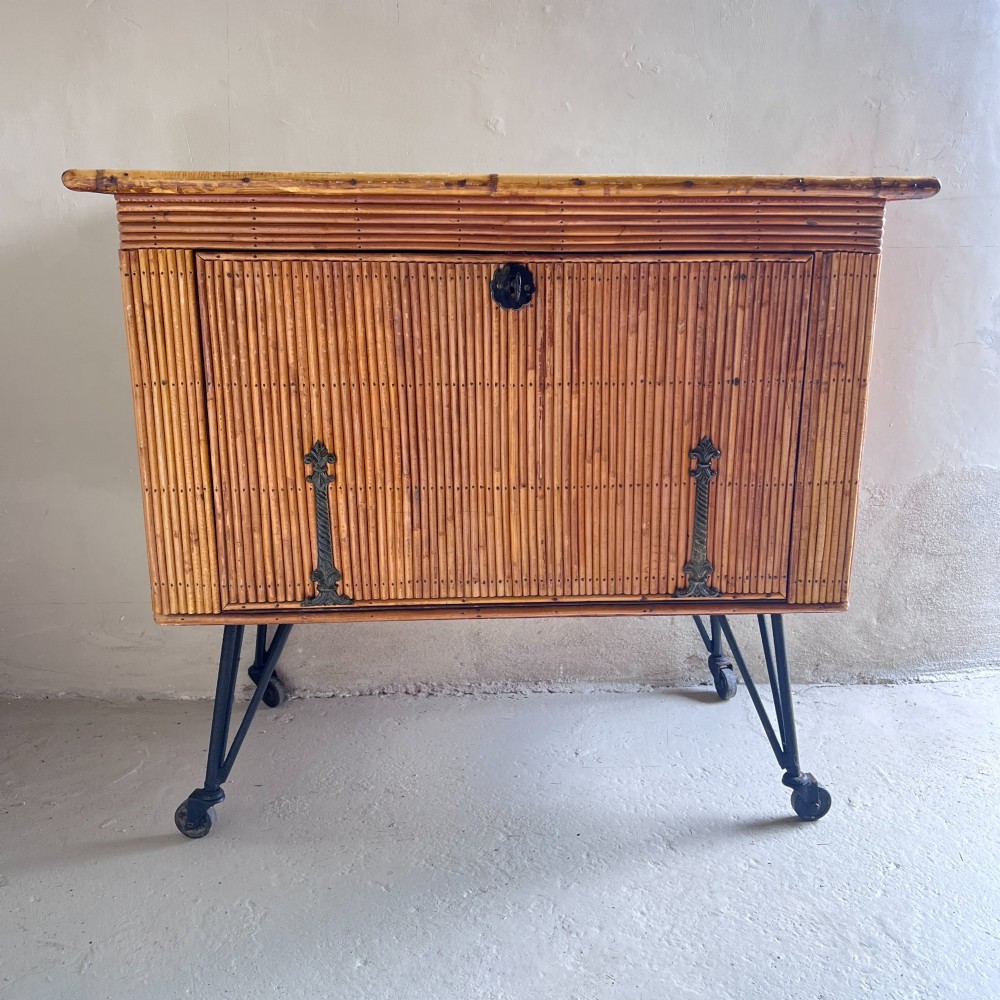 A French 1930s drinks cabinet featuring reeded bamboo panelling, decorative iron strap hinges, and black cast-iron legs with small wheel castors.