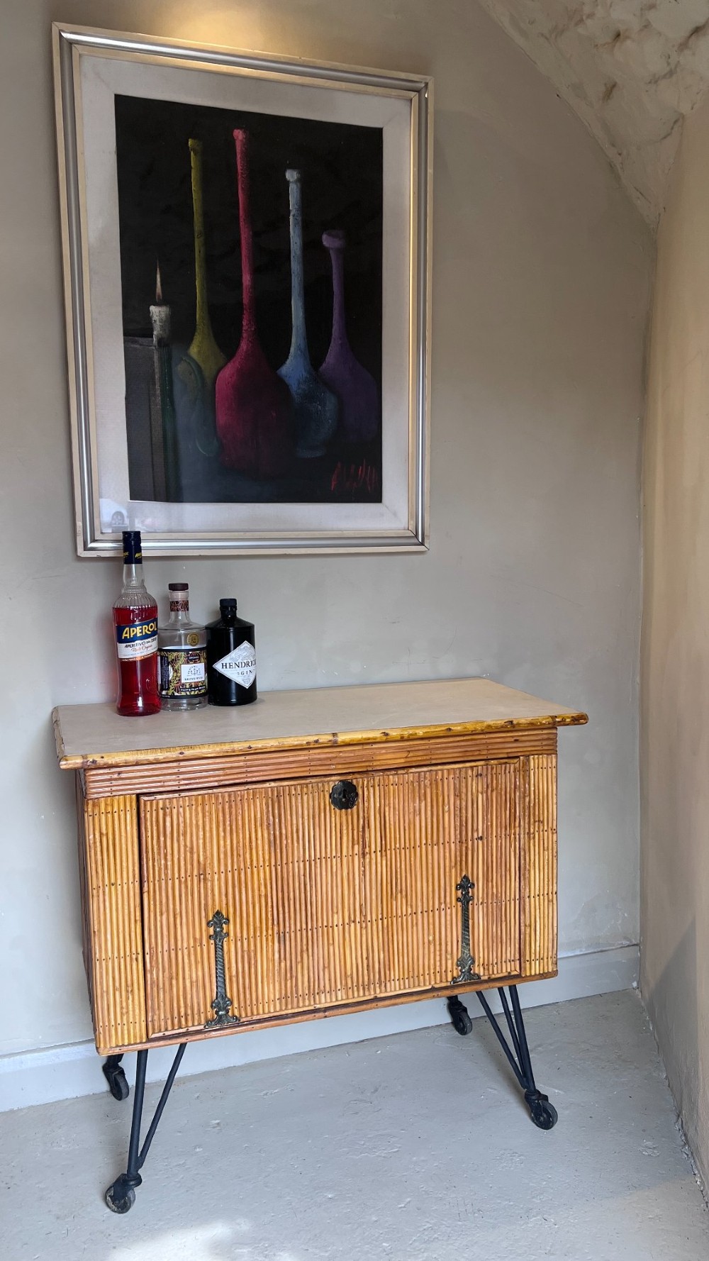 A French 1930s drinks cabinet featuring reeded bamboo panelling, decorative iron strap hinges, and black cast-iron legs with small wheel castors. View II