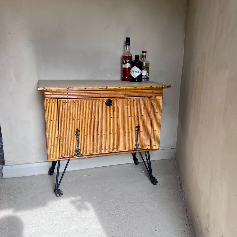 A French 1930s drinks cabinet featuring reeded bamboo panelling, decorative iron strap hinges, and black cast-iron legs with small wheel castors. View III