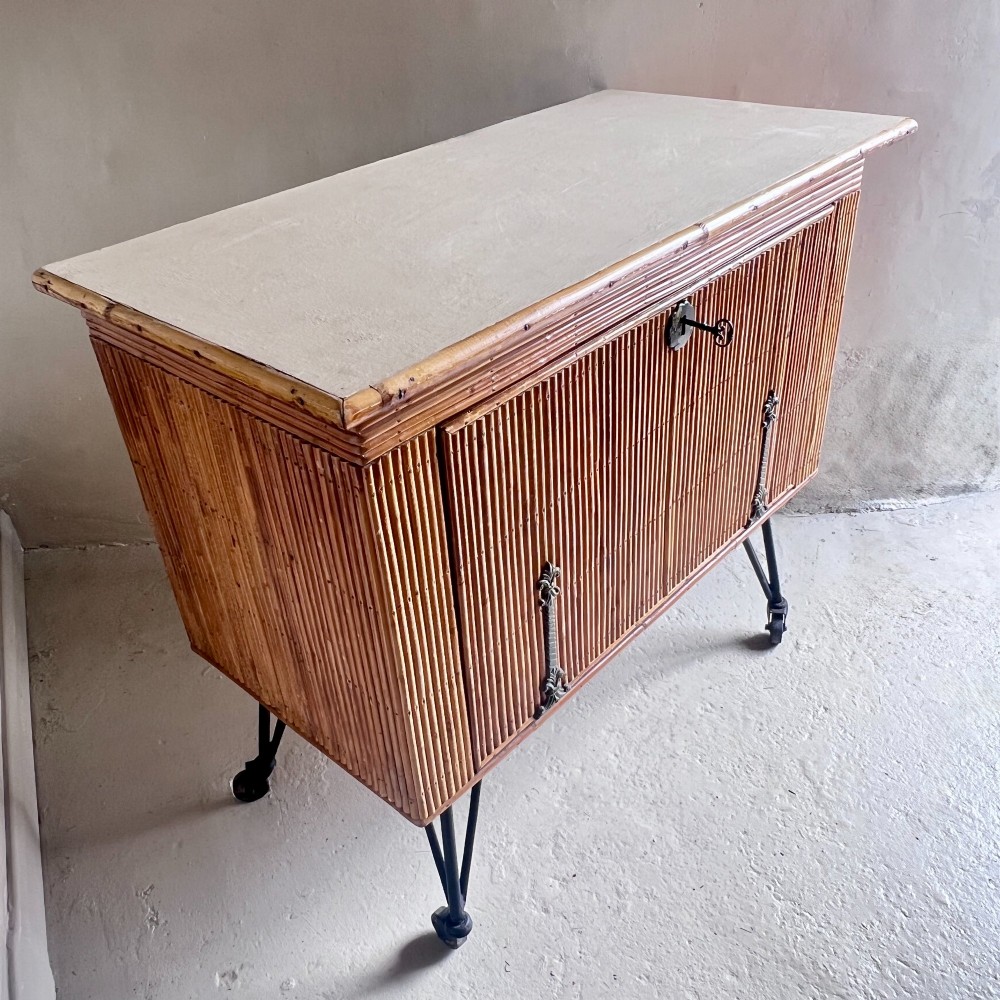 A French 1930s drinks cabinet featuring reeded bamboo panelling, decorative iron strap hinges, and black cast-iron legs with small wheel castors. View IV