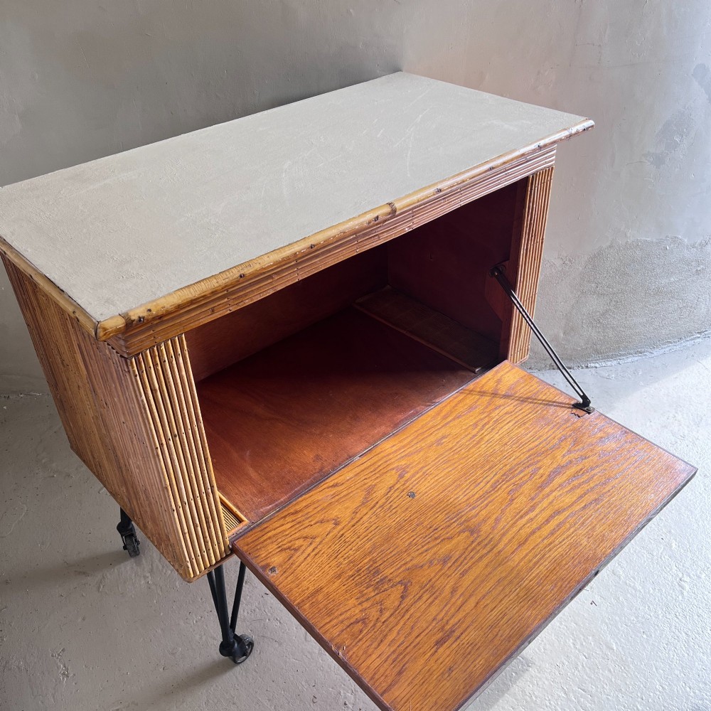 A French 1930s drinks cabinet featuring reeded bamboo panelling, decorative iron strap hinges, and black cast-iron legs with small wheel castors. View V