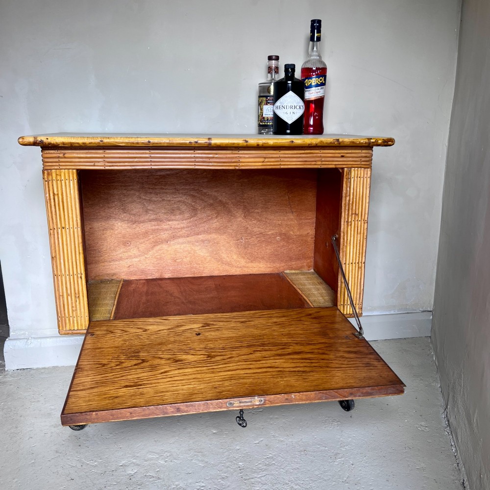 A French 1930s drinks cabinet featuring reeded bamboo panelling, decorative iron strap hinges, and black cast-iron legs with small wheel castors. View VI