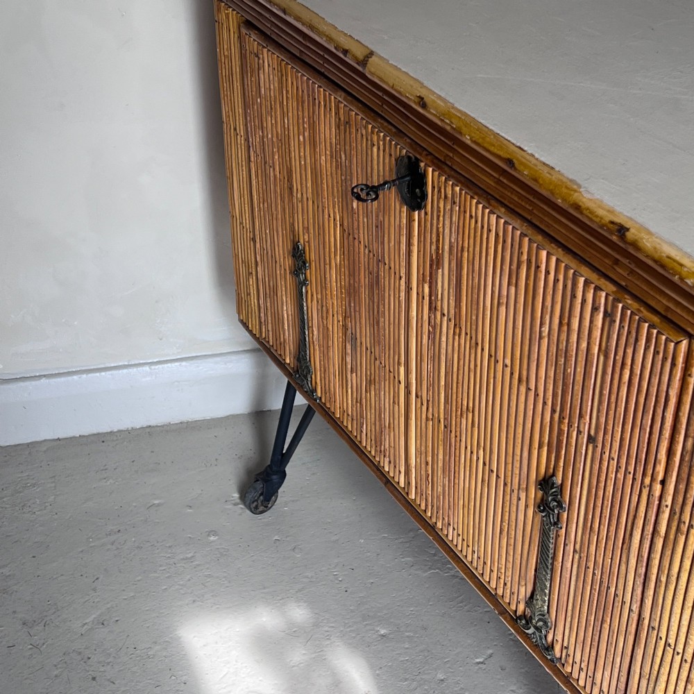 A French 1930s drinks cabinet featuring reeded bamboo panelling, decorative iron strap hinges, and black cast-iron legs with small wheel castors. View VII