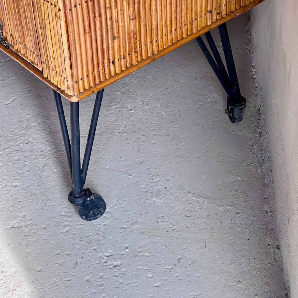 A French 1930s drinks cabinet featuring reeded bamboo panelling, decorative iron strap hinges, and black cast-iron legs with small wheel castors. View IX