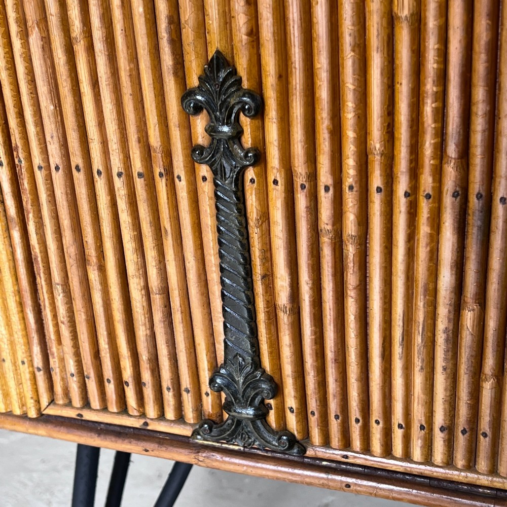 A French 1930s drinks cabinet featuring reeded bamboo panelling, decorative iron strap hinges, and black cast-iron legs with small wheel castors. View XI