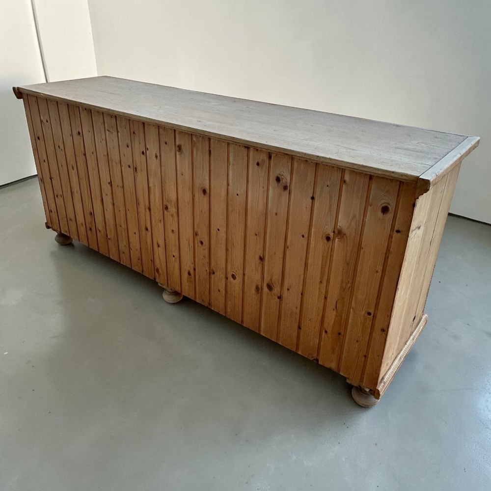 A large natural pine sideboard featuring two wide panelled doors with black metal handles and turned bun feet. View VII