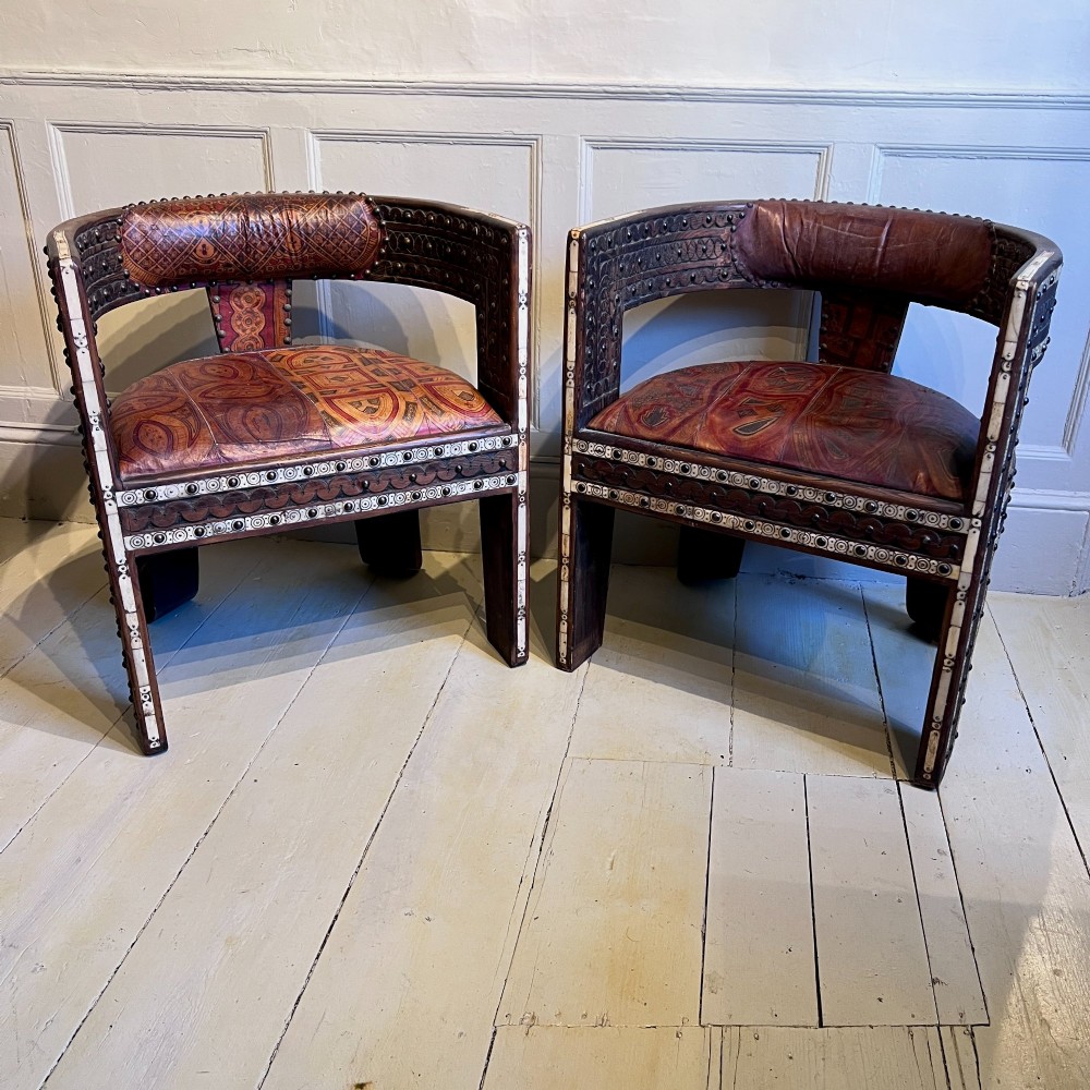 A pair of low curved hardwood armchairs featuring geometric bone inlay, brass stud detailing, and patterned red leather seats. View II