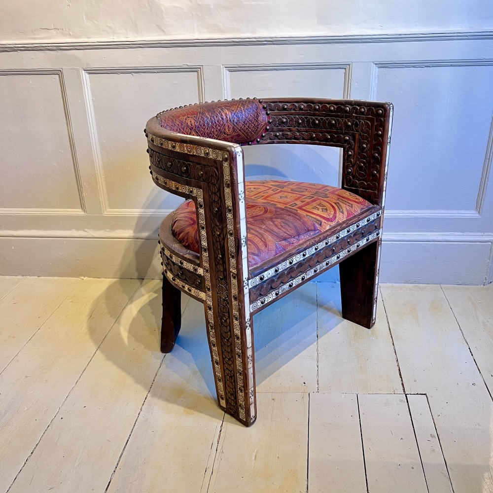 A pair of low curved hardwood armchairs featuring geometric bone inlay, brass stud detailing, and patterned red leather seats. View III