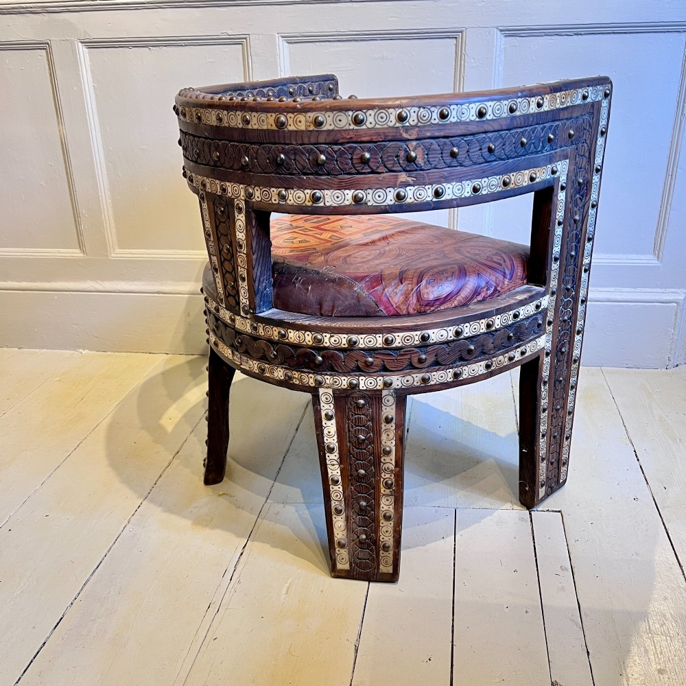 A pair of low curved hardwood armchairs featuring geometric bone inlay, brass stud detailing, and patterned red leather seats. View V