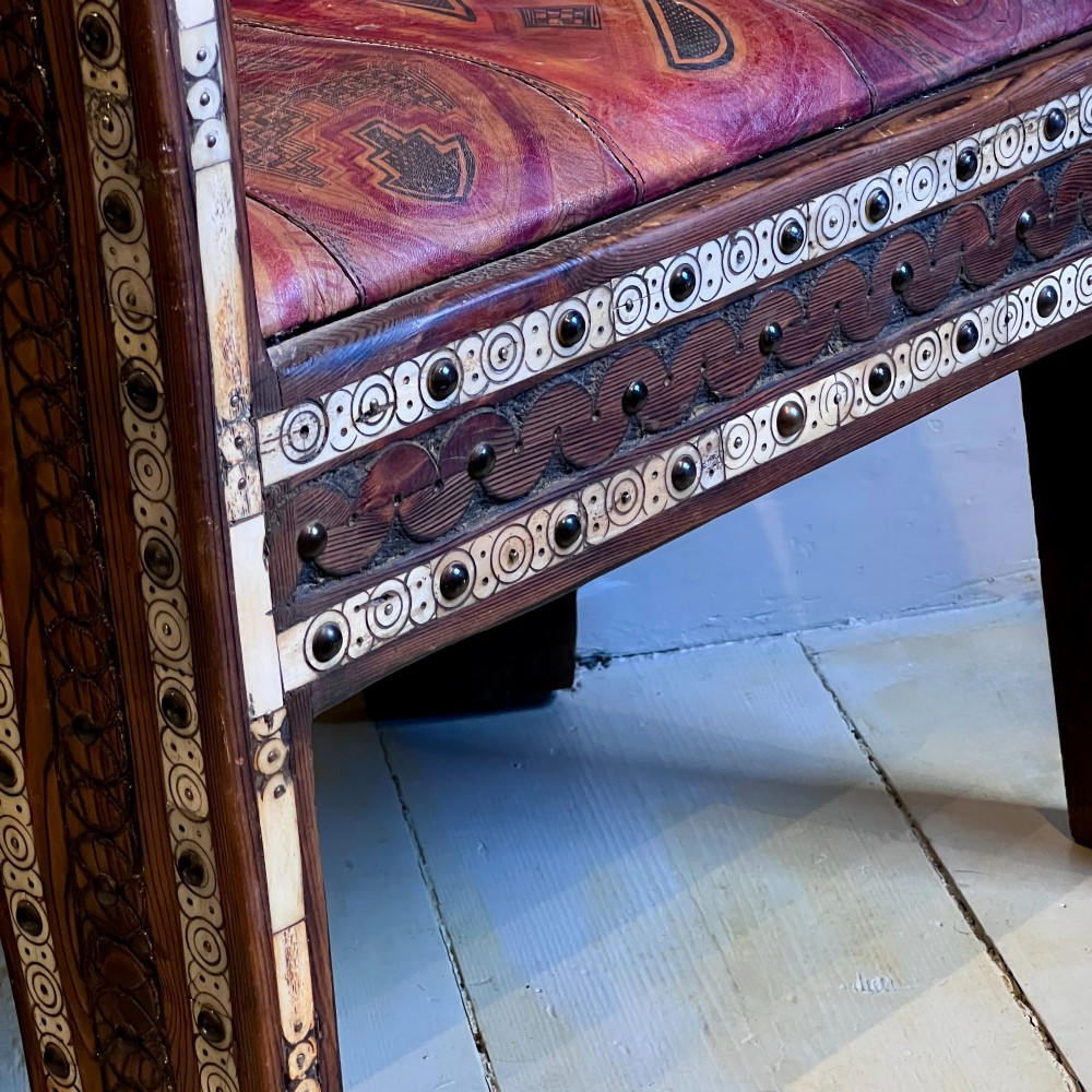 A pair of low curved hardwood armchairs featuring geometric bone inlay, brass stud detailing, and patterned red leather seats. View VI