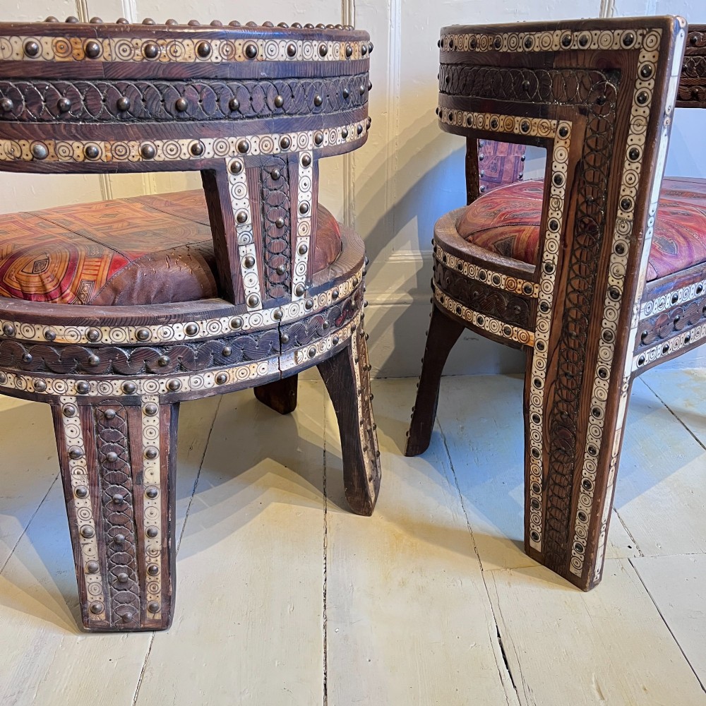 A pair of low curved hardwood armchairs featuring geometric bone inlay, brass stud detailing, and patterned red leather seats. View VII