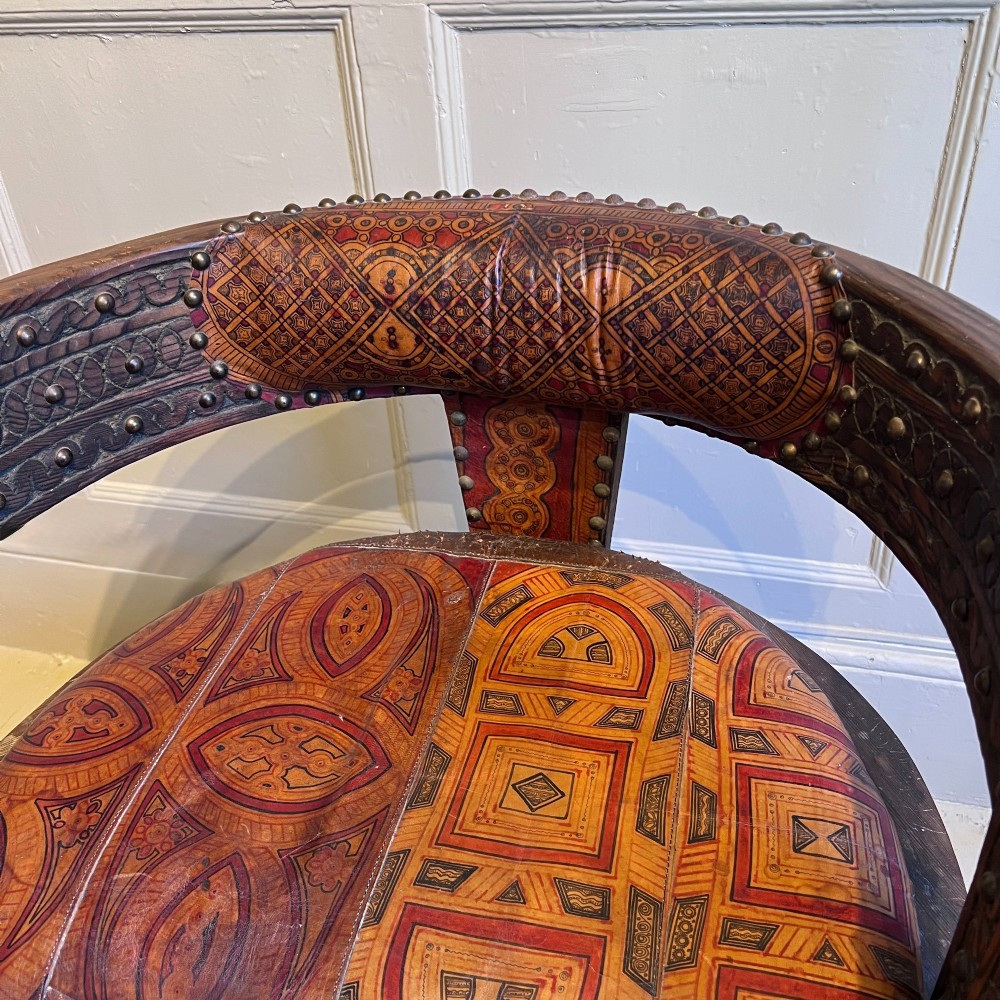 A pair of low curved hardwood armchairs featuring geometric bone inlay, brass stud detailing, and patterned red leather seats. View IX