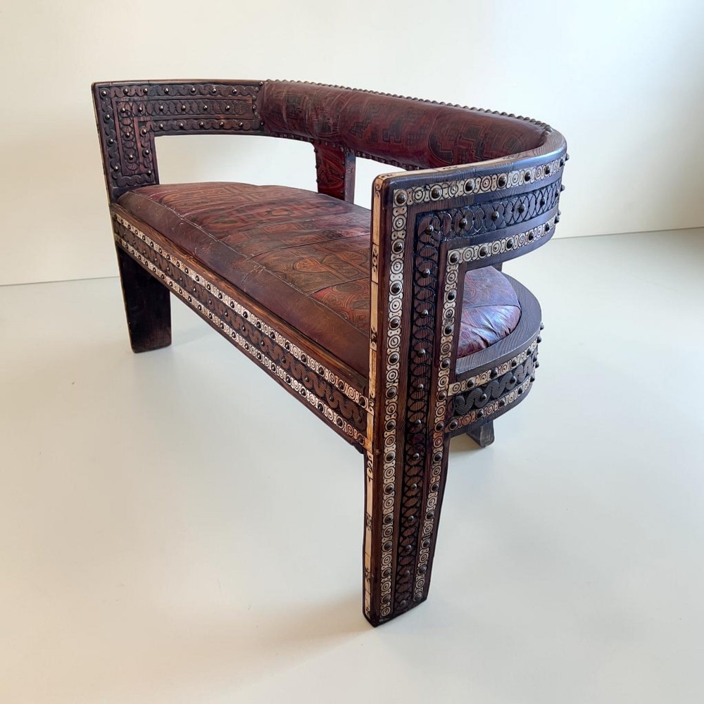 A pair of low curved hardwood armchairs featuring geometric bone inlay, brass stud detailing, and patterned red leather seats. View XI