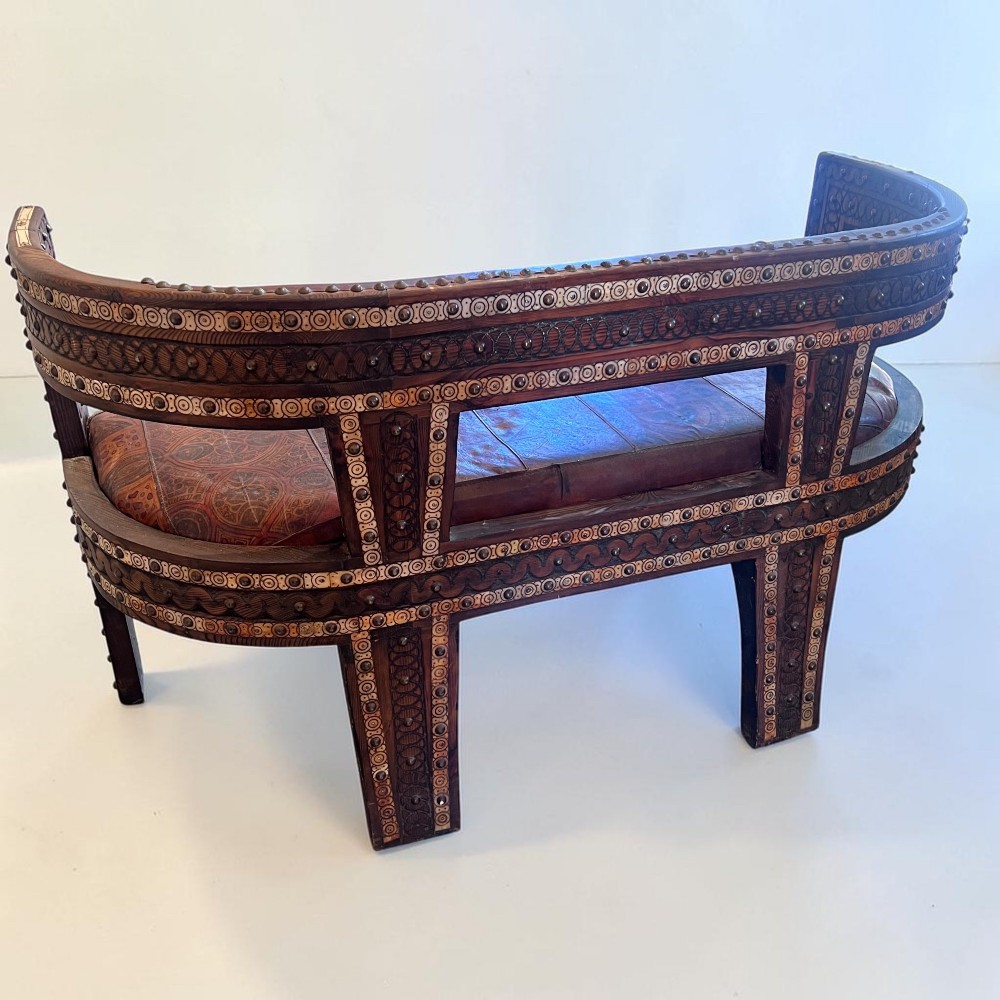 A pair of low curved hardwood armchairs featuring geometric bone inlay, brass stud detailing, and patterned red leather seats. View XII