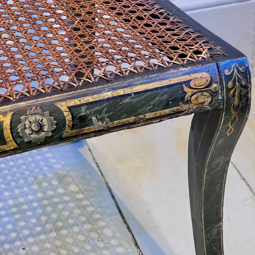 A pair of Regency period painted side chairs featuring woven cane seats, sabre legs, and gilt hand-painted detailing on a dark frame. View VI
