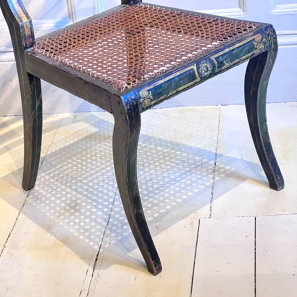 A pair of Regency period painted side chairs featuring woven cane seats, sabre legs, and gilt hand-painted detailing on a dark frame. View IX