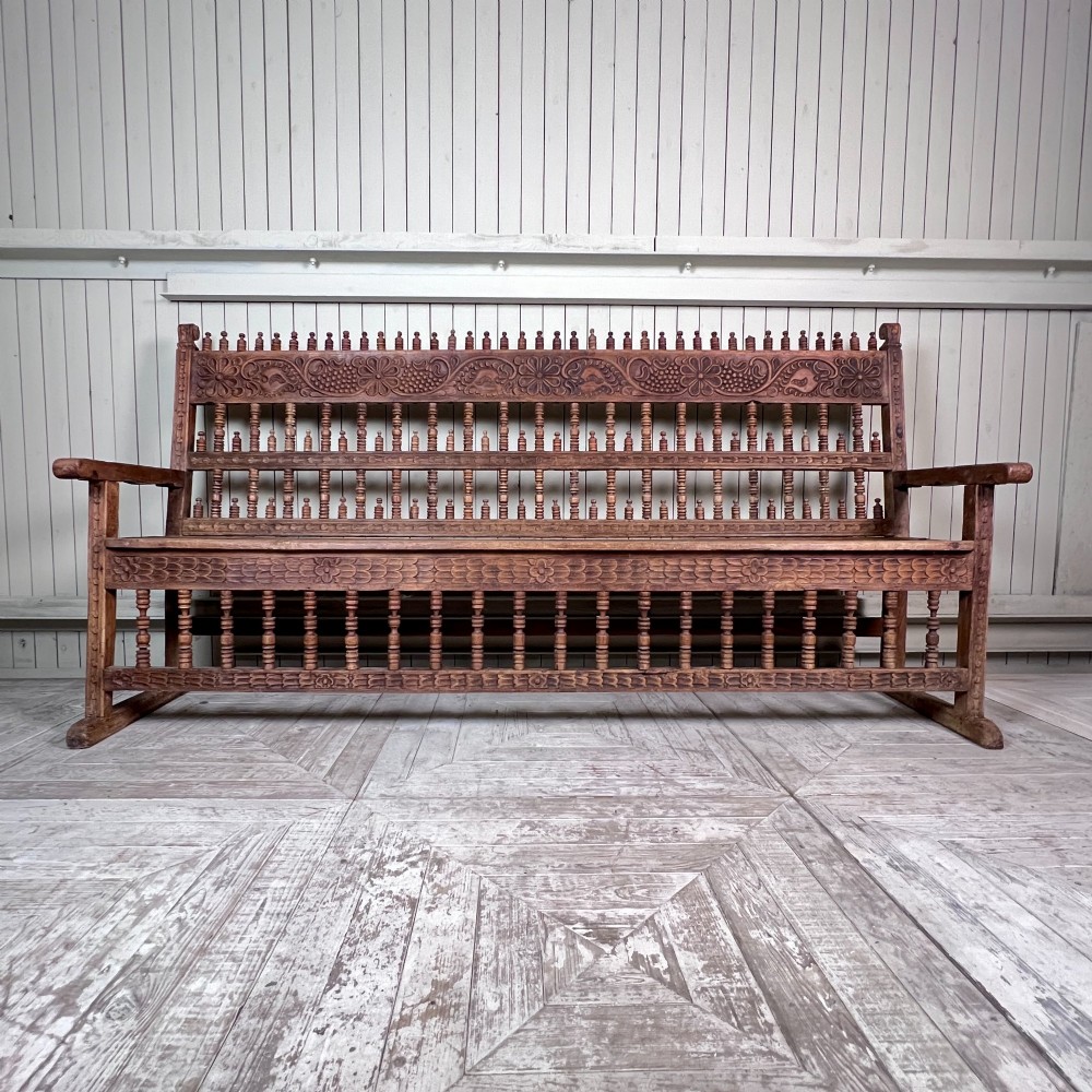 A large antique Spanish Colonial carved hardwood bench with floral relief carving and turned spindle details along the back and base. View II