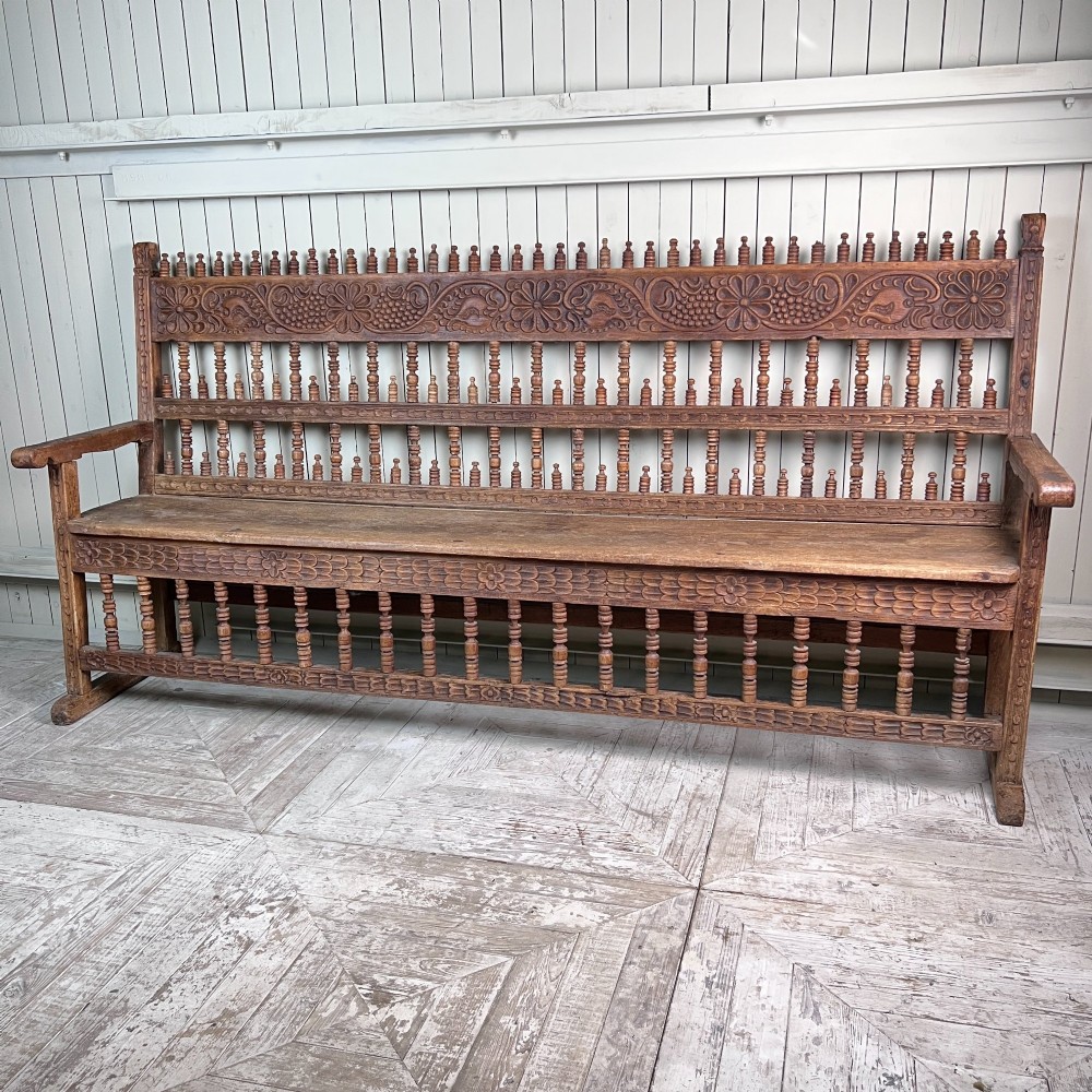 A large antique Spanish Colonial carved hardwood bench with floral relief carving and turned spindle details along the back and base. View V
