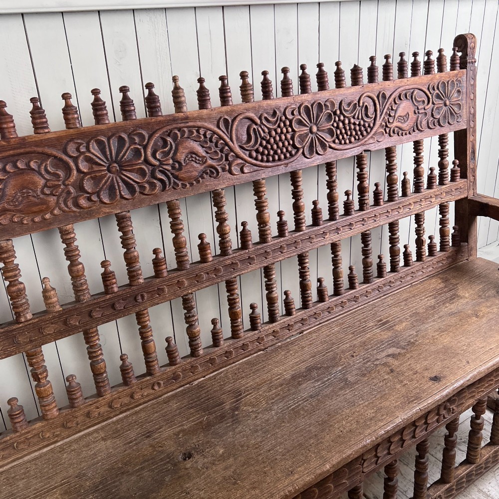 A large antique Spanish Colonial carved hardwood bench with floral relief carving and turned spindle details along the back and base. View VI