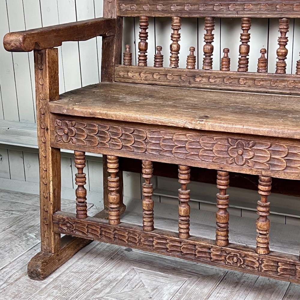 A large antique Spanish Colonial carved hardwood bench with floral relief carving and turned spindle details along the back and base. View VII