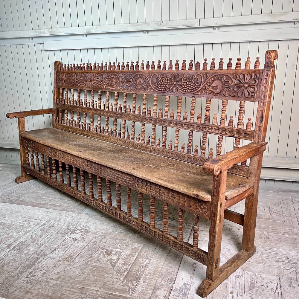 A large antique Spanish Colonial carved hardwood bench with floral relief carving and turned spindle details along the back and base. View IX