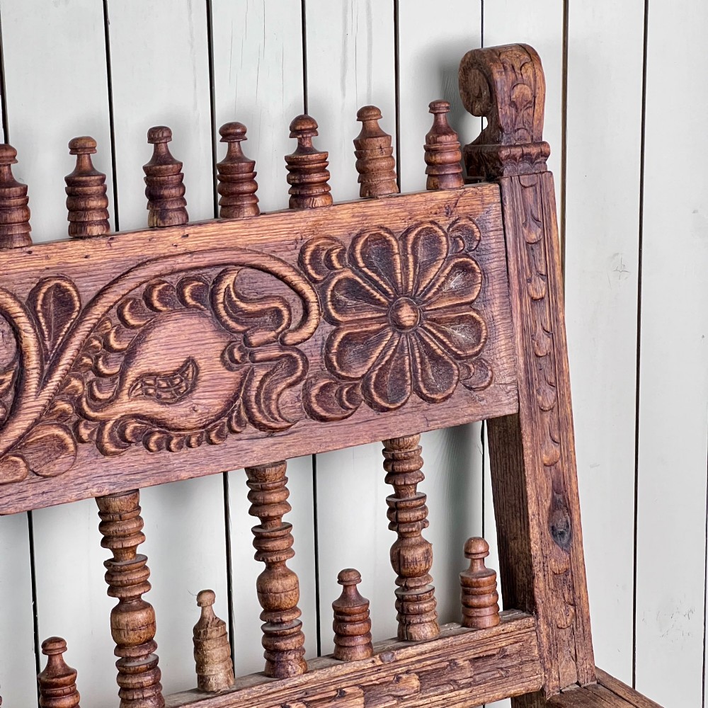 A large antique Spanish Colonial carved hardwood bench with floral relief carving and turned spindle details along the back and base. View X