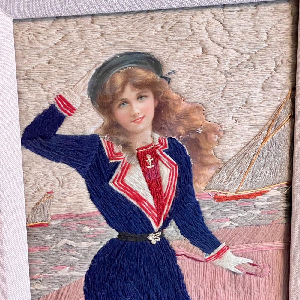 A framed Victorian woolwork picture depicting a sailor girl standing on a ship deck beside a Union Jack flag, enclosed within a rectangular frame decorated with natural sea shells. View VI