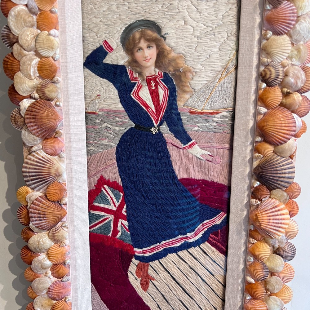 A framed Victorian woolwork picture depicting a sailor girl standing on a ship deck beside a Union Jack flag, enclosed within a rectangular frame decorated with natural sea shells. View VII
