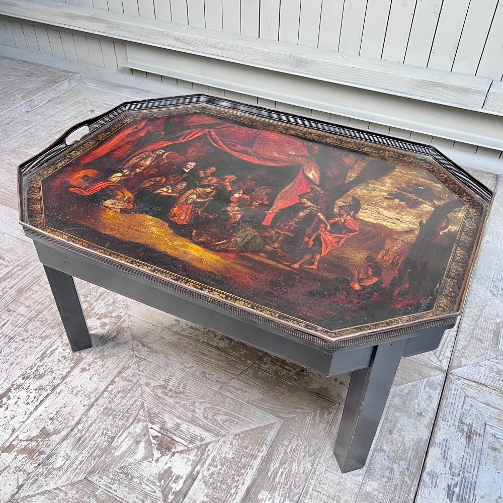 A nineteenth-century octagonal painted metal toleware tray table featuring a classical scene depicting the family of Darius before Alexander, set upon a dark wooden base.
