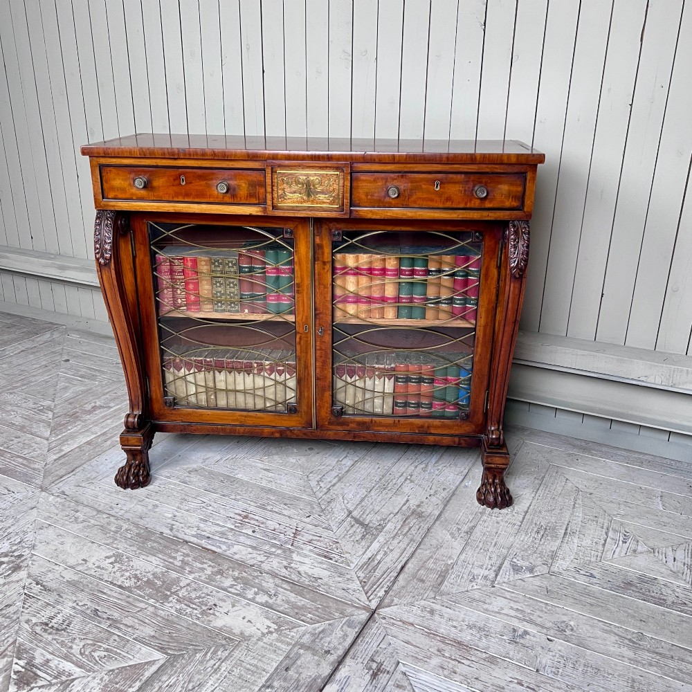 A Regency mahogany low chiffonier bookcase featuring brass wire grille doors, carved scroll supports terminating in paw feet, and brass inlay. View II