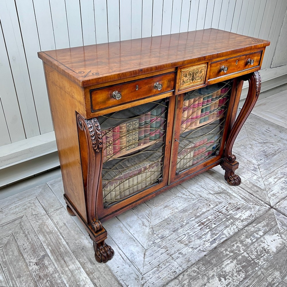 A Regency mahogany low chiffonier bookcase featuring brass wire grille doors, carved scroll supports terminating in paw feet, and brass inlay. View IV