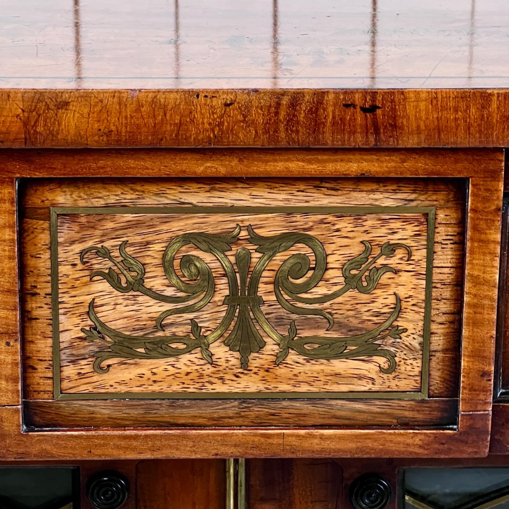 A Regency mahogany low chiffonier bookcase featuring brass wire grille doors, carved scroll supports terminating in paw feet, and brass inlay. View IX