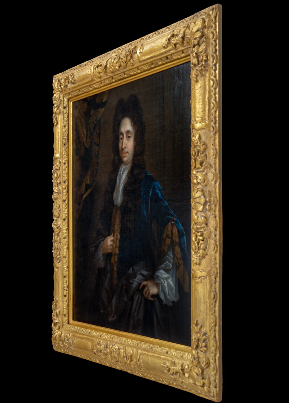 An oil painting of a 17th-century gentleman wearing a dark blue coat, full brown wig, and white lace cravat, set inside an ornate carved gilded frame. View II