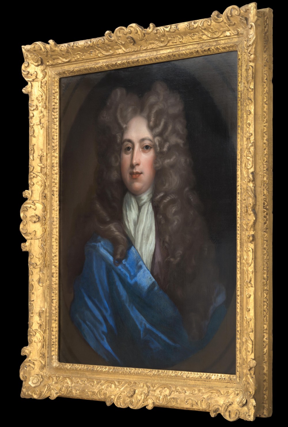 An oil on canvas portrait depicting a gentleman in a full brown periwig and draped blue cloak set within an oval spandrel and carved gold frame. View II