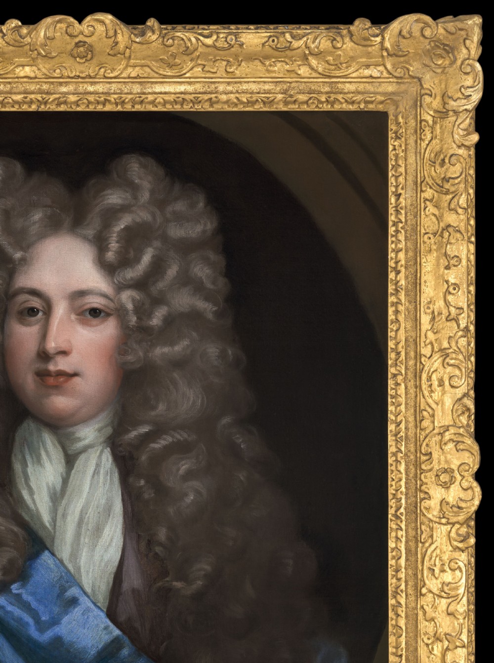 An oil on canvas portrait depicting a gentleman in a full brown periwig and draped blue cloak set within an oval spandrel and carved gold frame. View III
