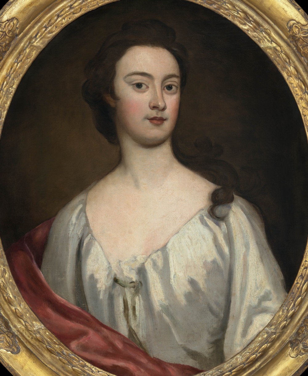 An eighteenth-century oval oil portrait depicting a young lady in a white gown and red mantle set inside a carved gilded frame. View II