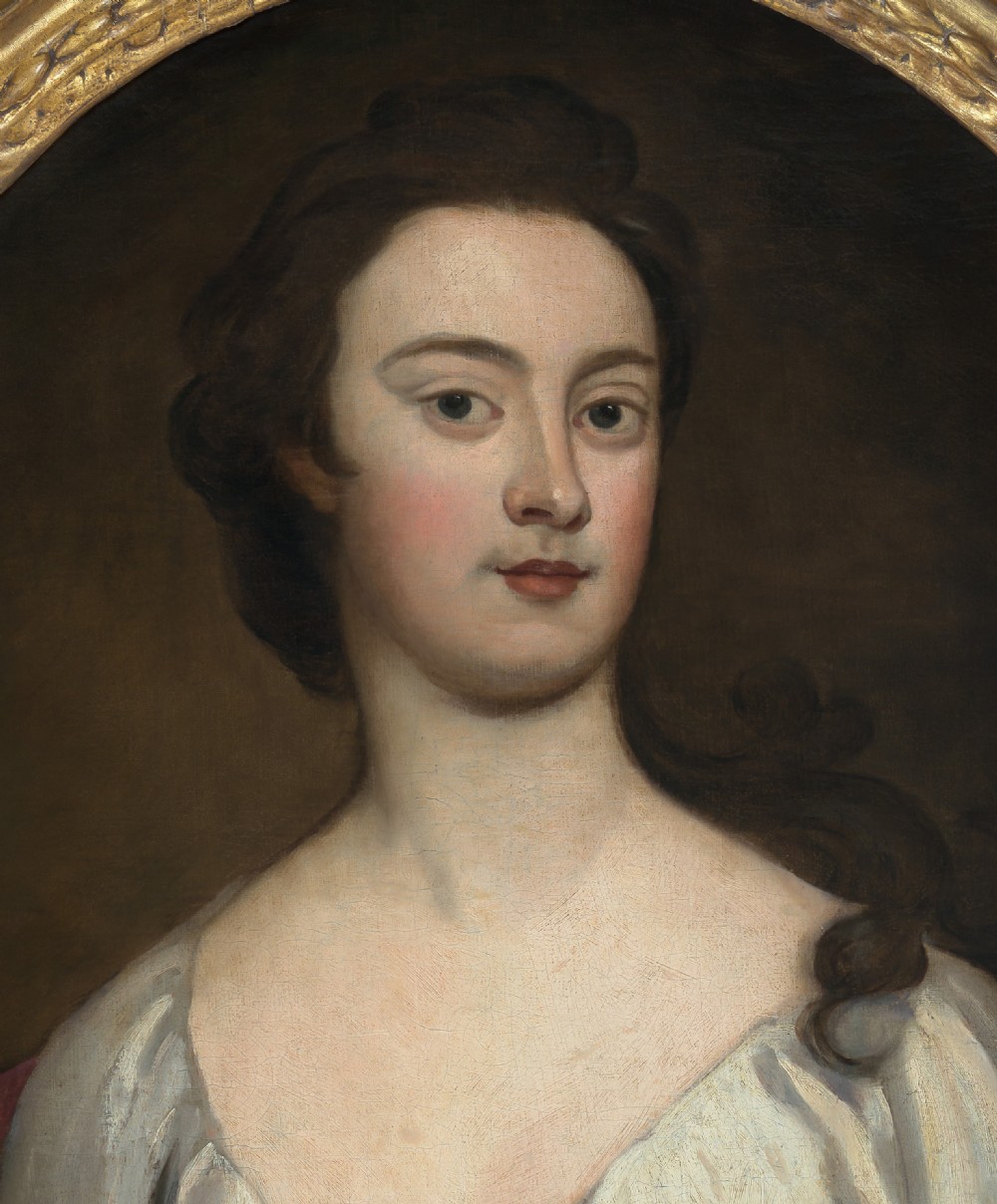An eighteenth-century oval oil portrait depicting a young lady in a white gown and red mantle set inside a carved gilded frame. View III