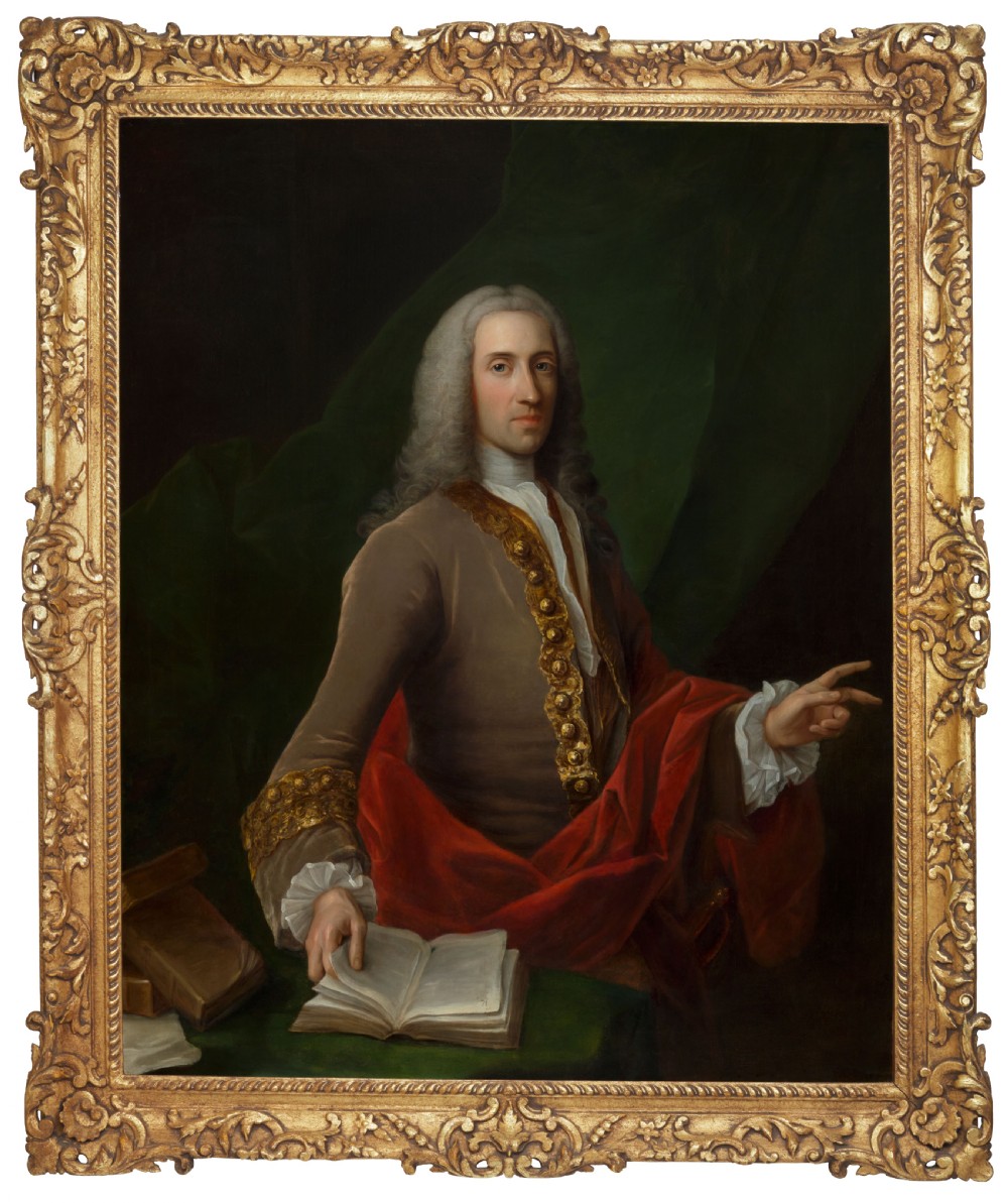 An 18th-century oil portrait depicting a wigged gentleman in a brown coat seated beside open books, enclosed in a carved giltwood frame.